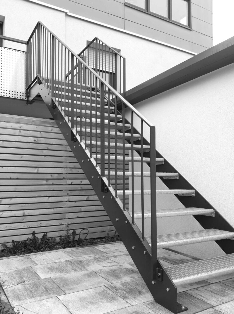 Metalltreppe neben Holzlattenzaun.
